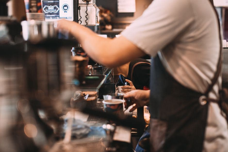 Een barista in schort bereidt koffie achter de toonbank van een sfeervolle koffiezaak.
