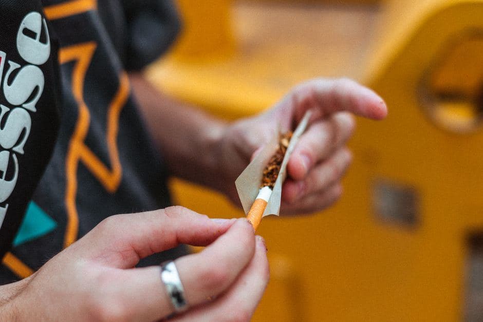 Handen draaien een joint met vloeipapier en een filter om wiet te roken.