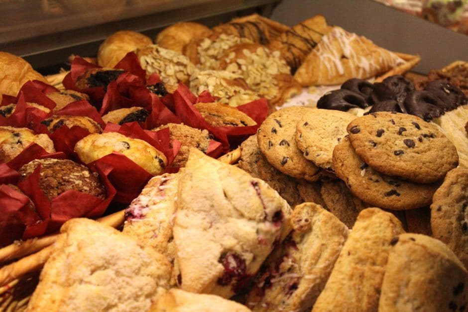 Versgebakken lekkernijen zoals chocoladekoekjes, muffins en zoete scones uitgestald in een vitrine.