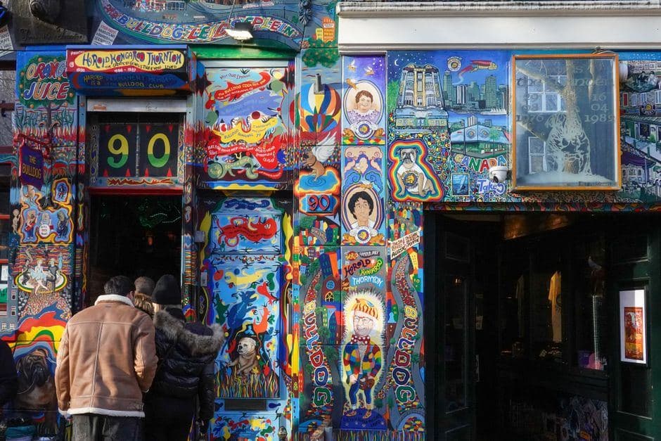 Bezoekers staan voor de kleurrijk beschilderde gevel en ingang van een bekende Amsterdamse coffeeshop.
