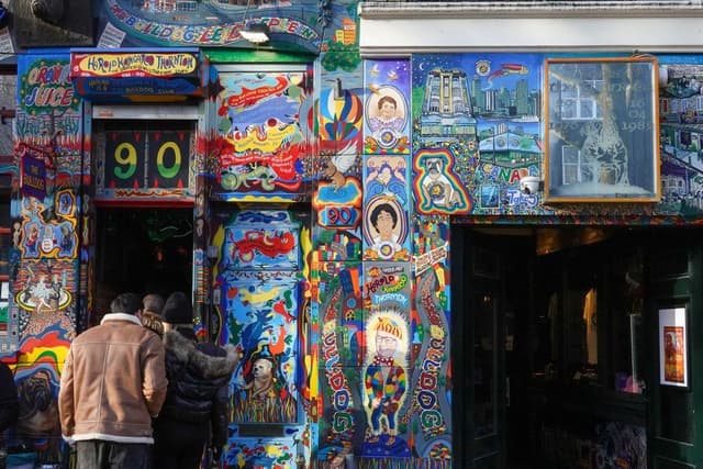 Bezoekers staan voor de kleurrijk beschilderde gevel en ingang van een bekende Amsterdamse coffeeshop.
