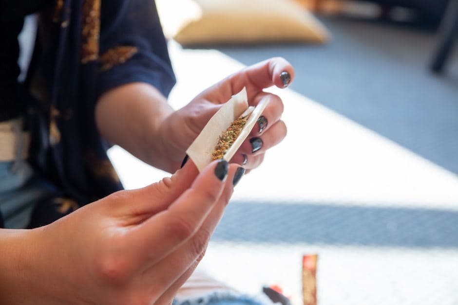 Handen met donkere nagellak rollen een joint gevuld met fijn gemalen wiet.