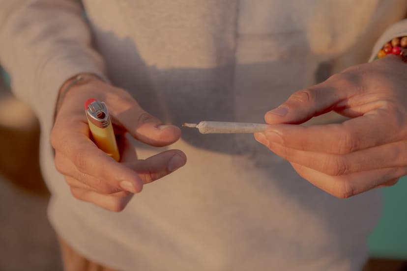 Iemand houdt een gele aansteker bij het uiteinde van een gedraaide joint om deze aan te steken in warm licht.