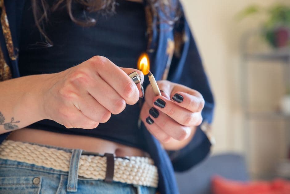 Iemand steekt met de vlam van een aansteker het uiteinde van een wietjoint aan.