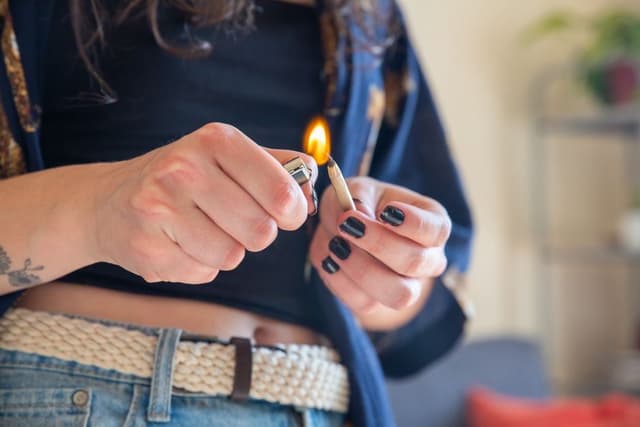 Iemand steekt met de vlam van een aansteker het uiteinde van een wietjoint aan.