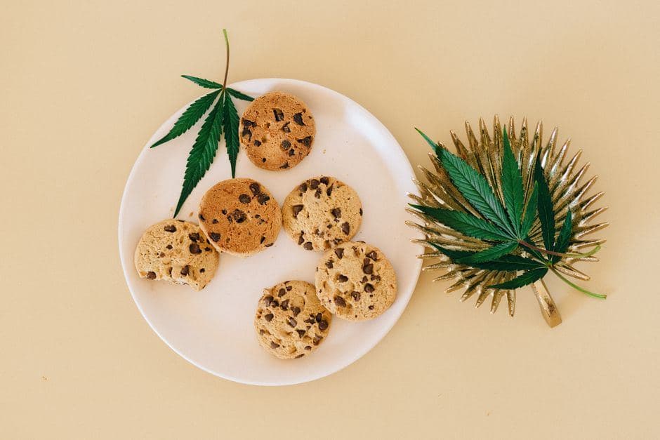 Wit bord met chocoladekoekjes met cannabis en verse wietbladeren op een beige achtergrond.