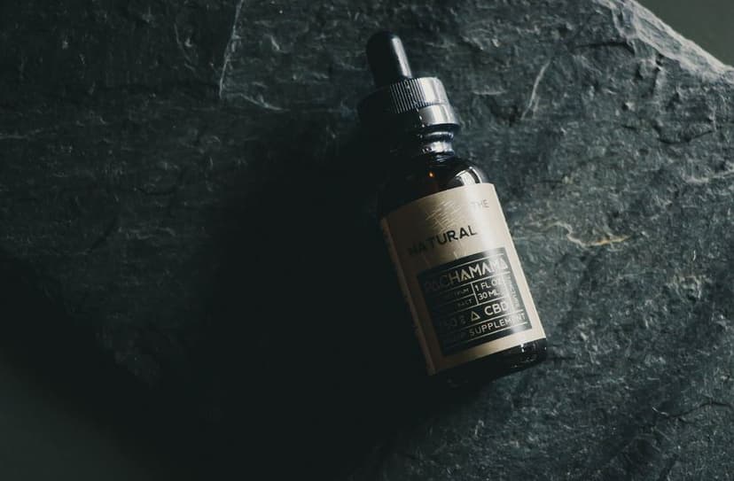Een bruin glazen pipetflesje met CBD-olie op een donkere, ruwe stenen ondergrond.
