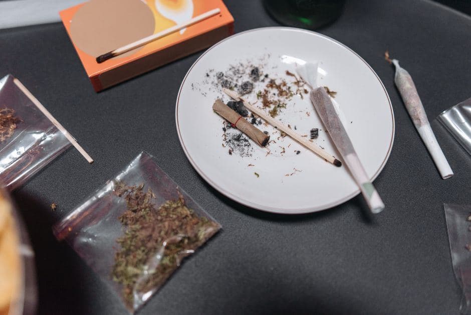 Zakjes wiet, gedraaide joints, as en lucifers op tafel die zorgen voor een sterke wietgeur in huis.