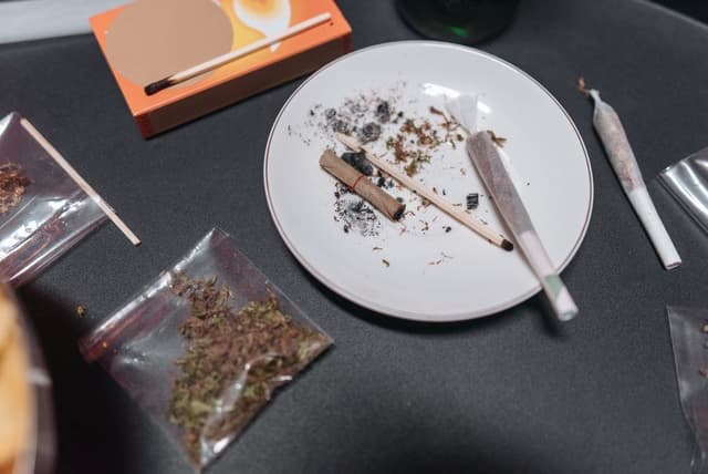 Zakjes wiet, gedraaide joints, as en lucifers op tafel die zorgen voor een sterke wietgeur in huis.