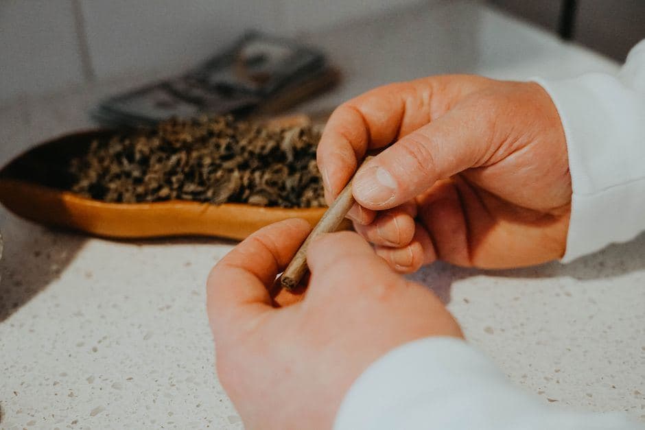 Handen die een pure joint rollen, met op de achtergrond een schaal gevuld met wiet en een stapeltje geld.