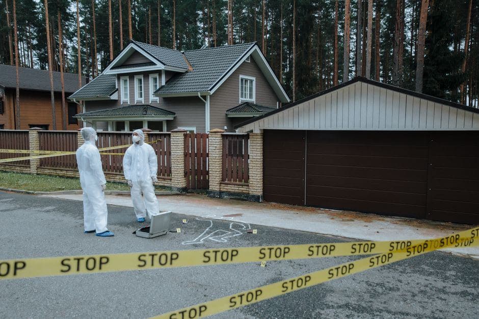 Forensisch onderzoekers in witte pakken doen onderzoek bij een krijtomtrek achter afzetlint voor een woning.