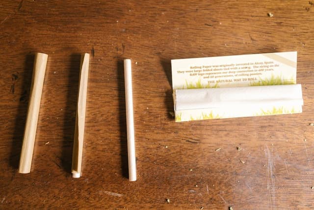 Drie opgerolde vloeitjes en een opengevouwen boekje vloei op een houten tafel naast elkaar